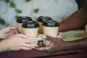 Coffee cups being exchanged in a standard takeaway tray, symbolizing the impersonal service of big coffee chains often chosen for birthday party catering. 